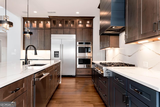 kitchen with a sink, dark wood finished floors, visible vents, wall chimney range hood, and appliances with stainless steel finishes