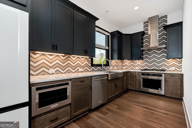 kitchen with a sink, stainless steel appliances, light countertops, dark wood-type flooring, and wall chimney exhaust hood