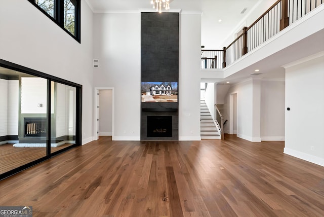 unfurnished living room featuring stairway, a towering ceiling, wood finished floors, baseboards, and a fireplace