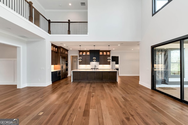 unfurnished living room with a sink, dark wood finished floors, visible vents, baseboards, and a towering ceiling