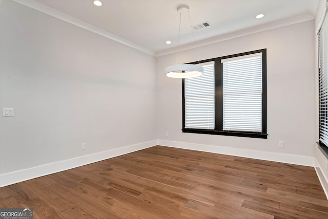 spare room featuring baseboards, wood finished floors, visible vents, and crown molding