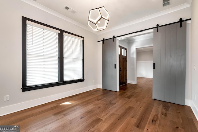 unfurnished dining area featuring a barn door, visible vents, wood finished floors, and crown molding