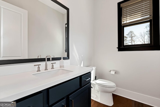 half bathroom with baseboards, wood finished floors, toilet, and vanity