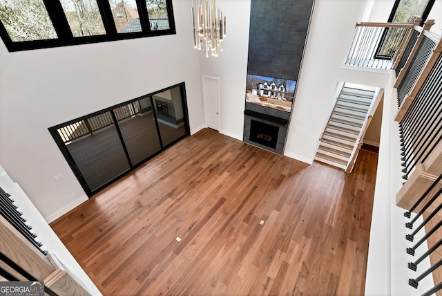 living room with a notable chandelier, wood finished floors, a fireplace, baseboards, and stairs