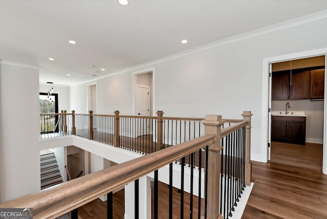 hallway with recessed lighting, dark wood-style floors, ornamental molding, a sink, and an upstairs landing