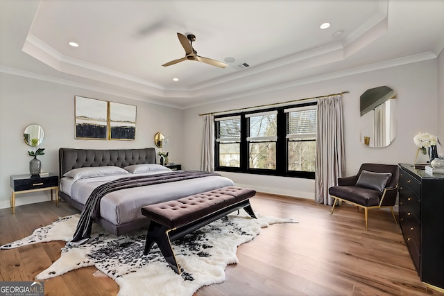 bedroom with a tray ceiling, wood finished floors, visible vents, and crown molding