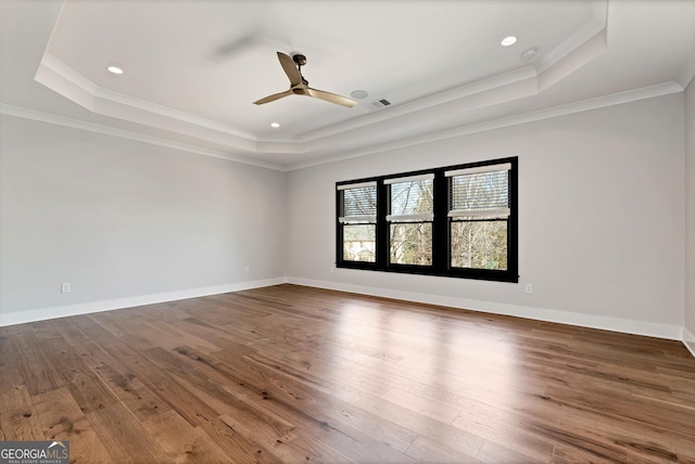 empty room featuring a ceiling fan, dark wood-style flooring, a tray ceiling, and visible vents