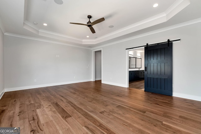 unfurnished bedroom featuring a barn door, ornamental molding, wood finished floors, and a raised ceiling