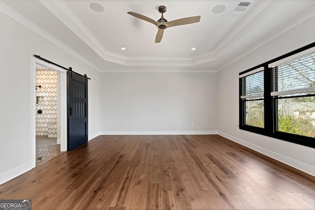 unfurnished bedroom featuring a barn door, crown molding, wood finished floors, a tray ceiling, and visible vents