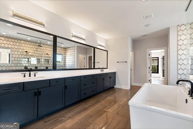 full bathroom with double vanity, a freestanding tub, visible vents, and a sink