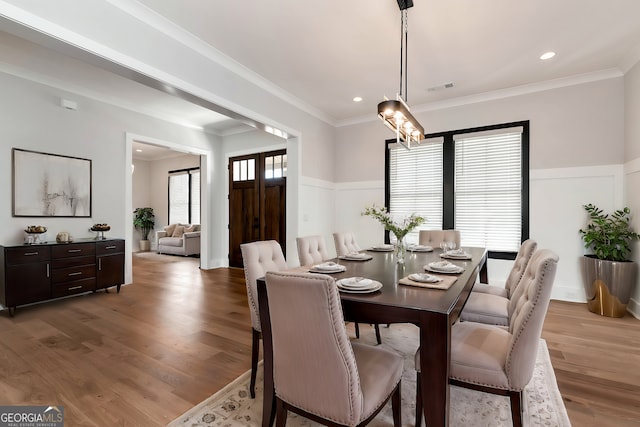 dining area with light wood-type flooring, visible vents, a wainscoted wall, and ornamental molding