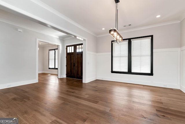 unfurnished dining area with crown molding, wood finished floors, wainscoting, an inviting chandelier, and visible vents