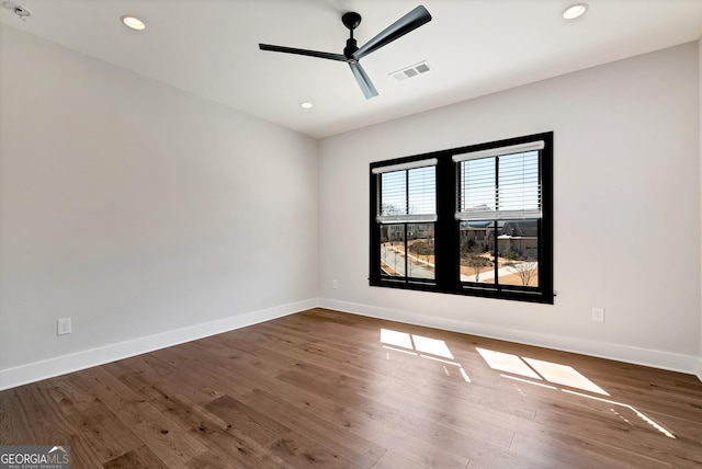 empty room with wood finished floors, baseboards, a ceiling fan, and visible vents