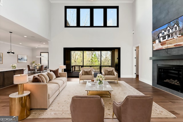 living area with wood finished floors, recessed lighting, a large fireplace, baseboards, and a towering ceiling