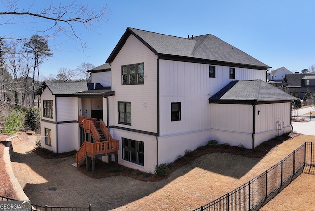 back of house featuring a shingled roof, stairs, and fence