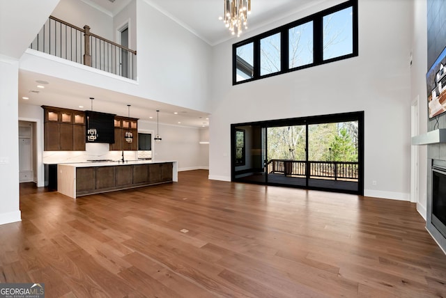 unfurnished living room with wood finished floors, baseboards, ornamental molding, a tiled fireplace, and a notable chandelier