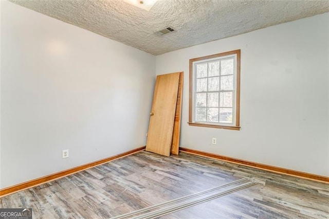 spare room featuring visible vents, a textured ceiling, baseboards, and wood finished floors