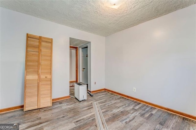 unfurnished bedroom featuring a closet, a textured ceiling, baseboards, and wood finished floors