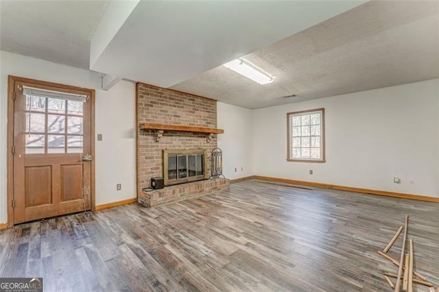 unfurnished living room featuring a fireplace, wood finished floors, baseboards, and a textured ceiling