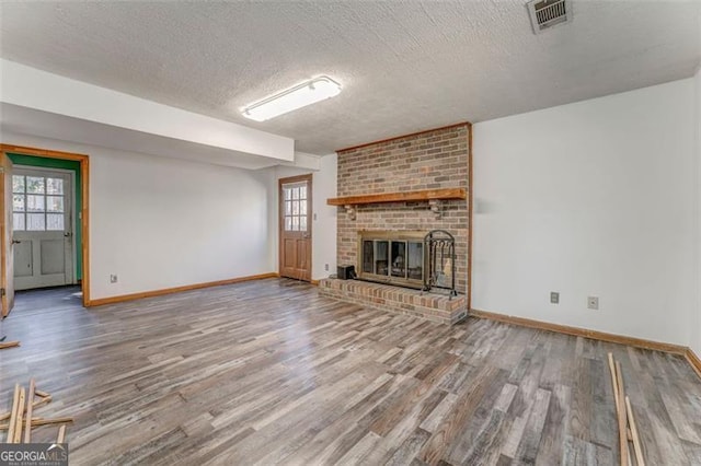 unfurnished living room with visible vents, a textured ceiling, wood finished floors, baseboards, and a brick fireplace