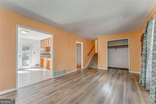 unfurnished living room featuring visible vents, a textured ceiling, wood finished floors, and stairway