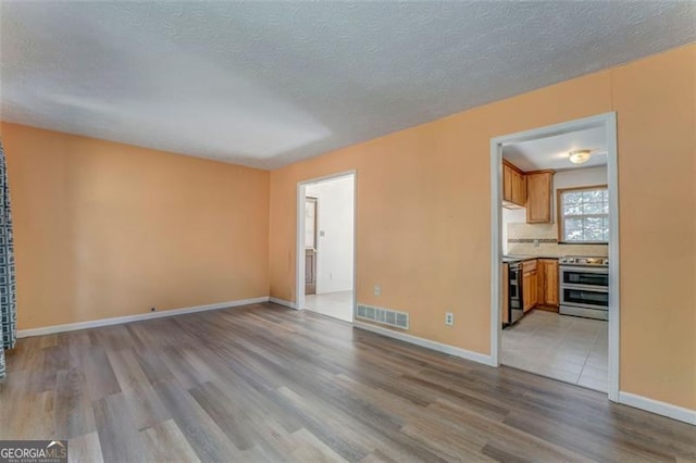 unfurnished living room featuring visible vents, baseboards, a textured ceiling, and wood finished floors