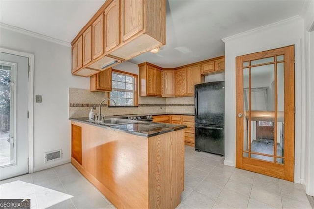 kitchen featuring visible vents, a sink, backsplash, freestanding refrigerator, and a peninsula