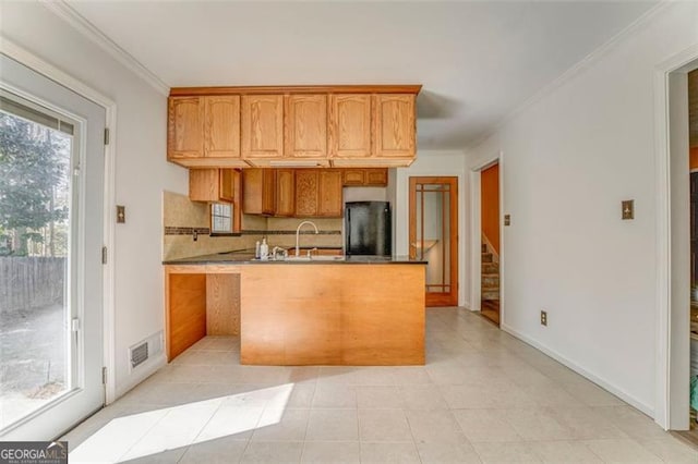 kitchen with visible vents, a sink, decorative backsplash, ornamental molding, and black refrigerator