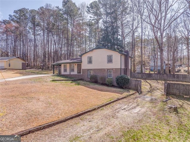 tri-level home with brick siding, dirt driveway, a front lawn, and fence