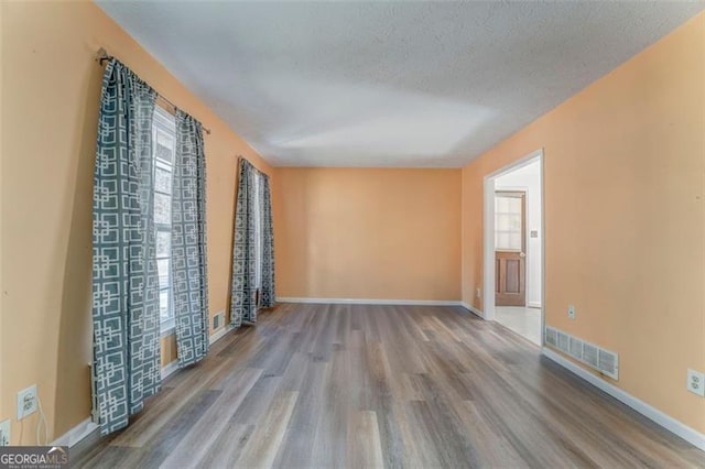 unfurnished room featuring baseboards, wood finished floors, visible vents, and a textured ceiling