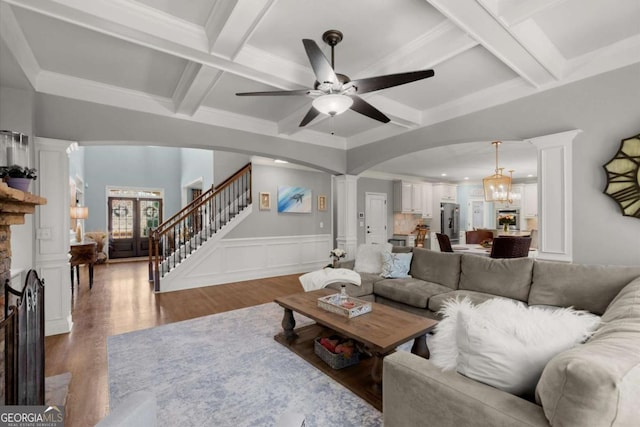 living area with coffered ceiling, ceiling fan with notable chandelier, arched walkways, and ornate columns