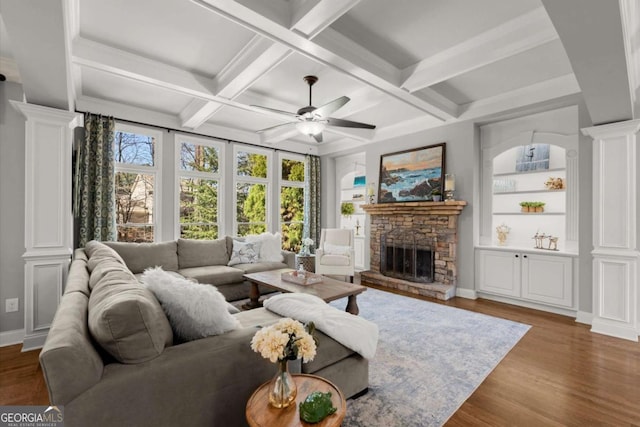 living room with built in shelves, wood finished floors, a stone fireplace, decorative columns, and ceiling fan