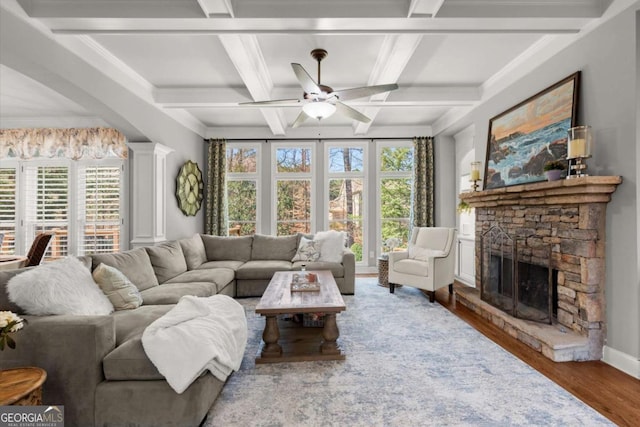 living area with wood finished floors, coffered ceiling, a fireplace, ceiling fan, and beamed ceiling