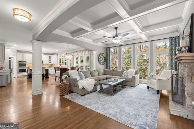 living room with decorative columns, beamed ceiling, wood finished floors, and ceiling fan with notable chandelier