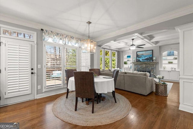 dining space with ceiling fan, beam ceiling, a stone fireplace, wood finished floors, and coffered ceiling