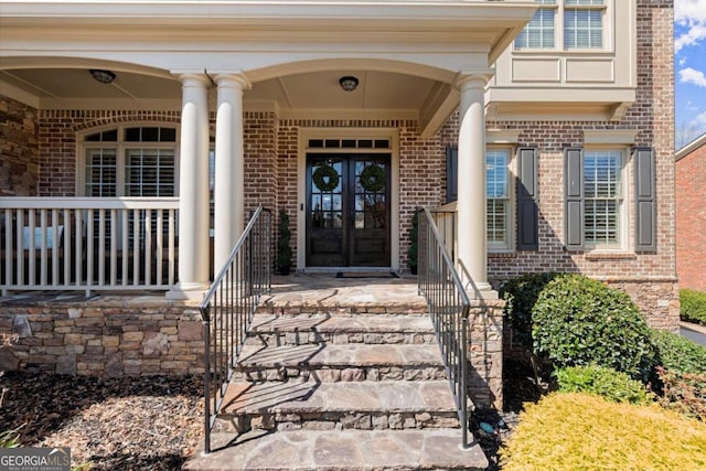 entrance to property with a porch, french doors, and brick siding