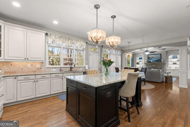 kitchen featuring a stone fireplace, ceiling fan with notable chandelier, white cabinetry, and a sink