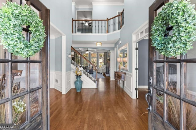 entrance foyer with stairway, wood finished floors, a ceiling fan, a wainscoted wall, and crown molding