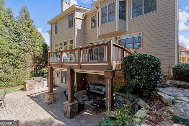 rear view of house with exterior kitchen, a wooden deck, a patio area, and a chimney