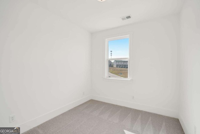 spare room featuring visible vents, light colored carpet, and baseboards