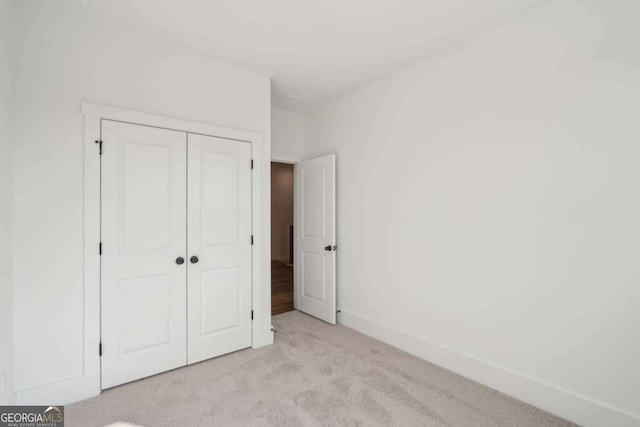 unfurnished bedroom with a closet, light colored carpet, and baseboards