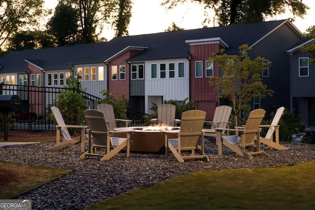 back of property at dusk with board and batten siding, an outdoor fire pit, and fence