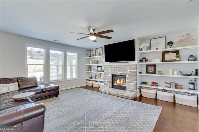 living room featuring wood finished floors, baseboards, visible vents, a ceiling fan, and a stone fireplace