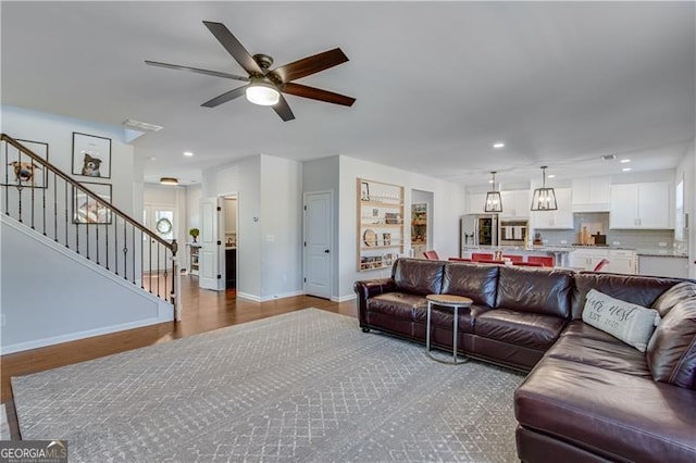 living room featuring stairway, wood finished floors, baseboards, and ceiling fan