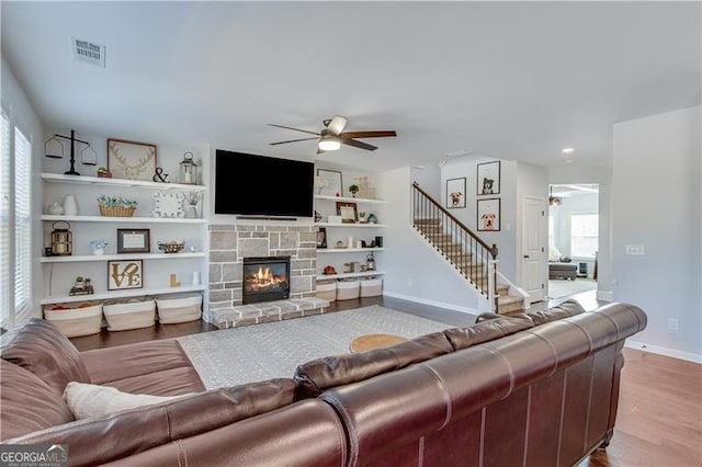 living area featuring a stone fireplace, stairway, a ceiling fan, and visible vents