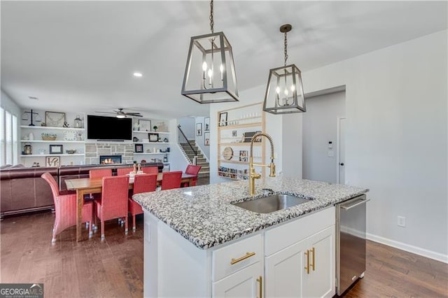 kitchen with a sink, dishwasher, a fireplace, a ceiling fan, and dark wood-style flooring