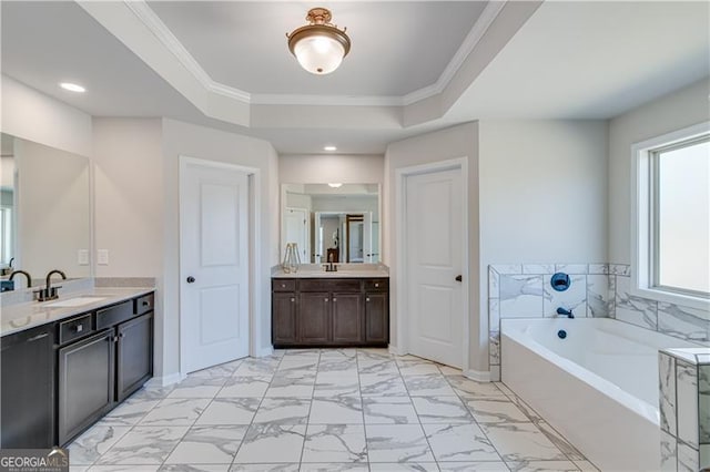 bathroom with two vanities, a raised ceiling, a garden tub, and ornamental molding