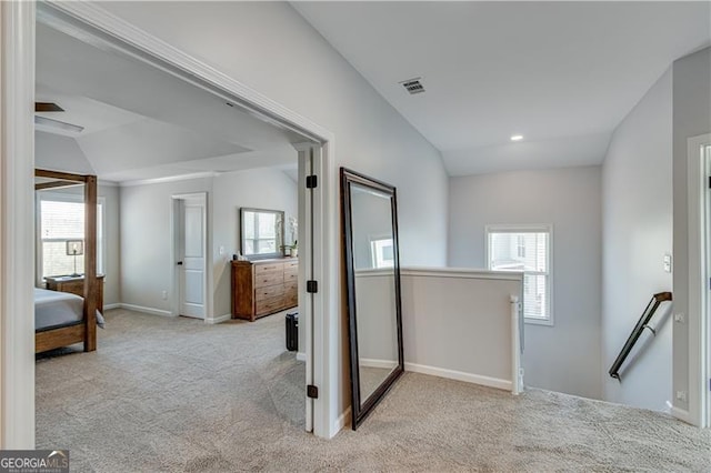 hallway with visible vents, baseboards, lofted ceiling, carpet floors, and an upstairs landing