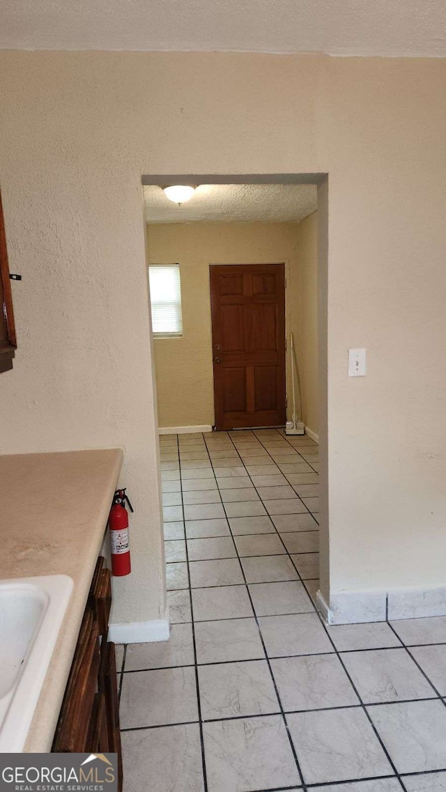 hallway with light tile patterned floors, baseboards, and a sink