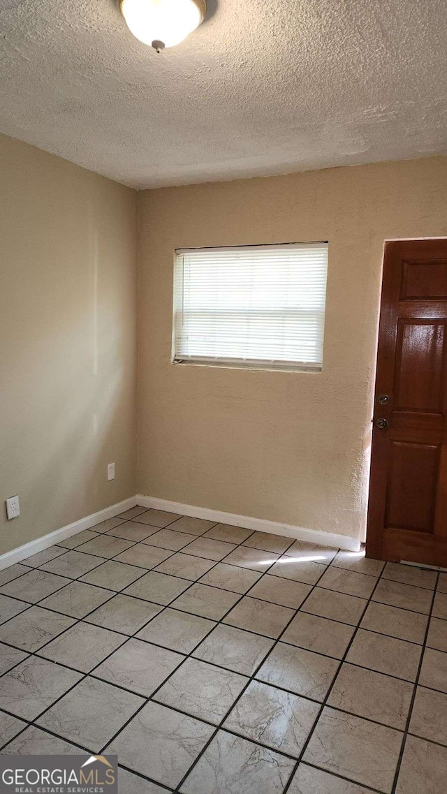 unfurnished room with light tile patterned flooring, baseboards, and a textured ceiling